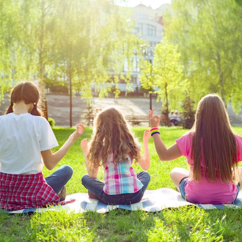 Three young girls doing yoga pose outdoor, yoga at sunset in the park, back view