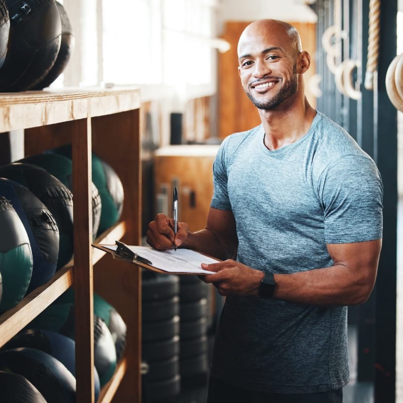 Portrait, clipboard and planning with man in gym for fitness instructor, inventory and membership record. Workout schedule, personal trainer and equipment supervisor with person in health facility.